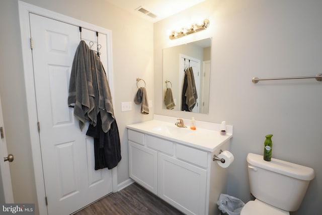 half bathroom featuring visible vents, wood finished floors, toilet, and vanity
