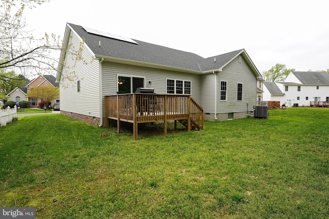 rear view of house featuring cooling unit, roof mounted solar panels, a deck, and a lawn