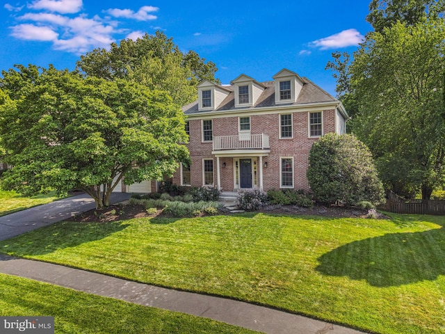 colonial inspired home featuring fence, concrete driveway, a front lawn, and brick siding
