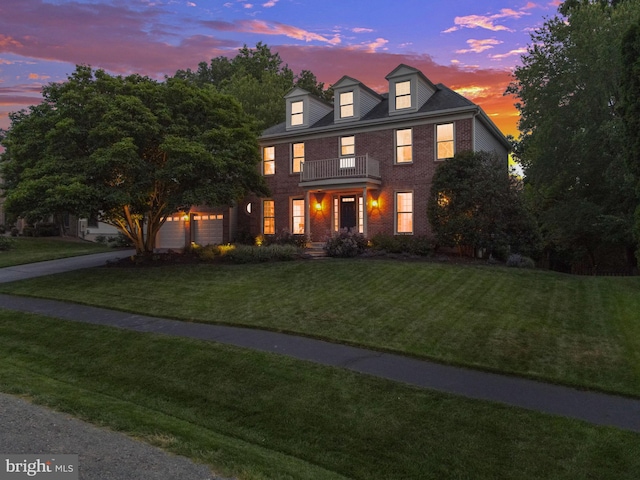 colonial inspired home with an attached garage, a balcony, brick siding, a lawn, and driveway