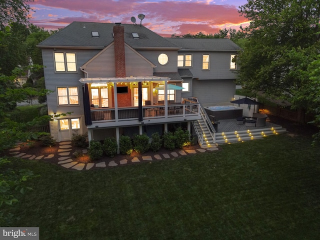 back of property at dusk with a hot tub, a wooden deck, a fenced backyard, a chimney, and a lawn