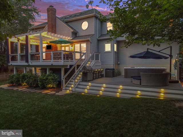 back of house at dusk featuring a lawn, a deck, a hot tub, and a pergola