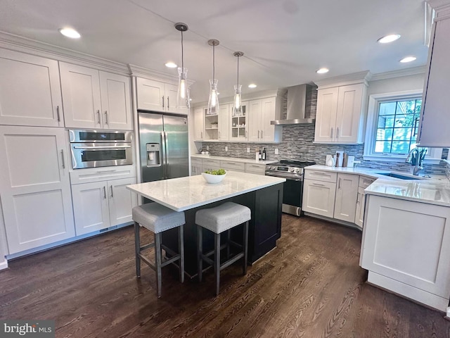 kitchen featuring appliances with stainless steel finishes, white cabinetry, a sink, ornamental molding, and wall chimney exhaust hood