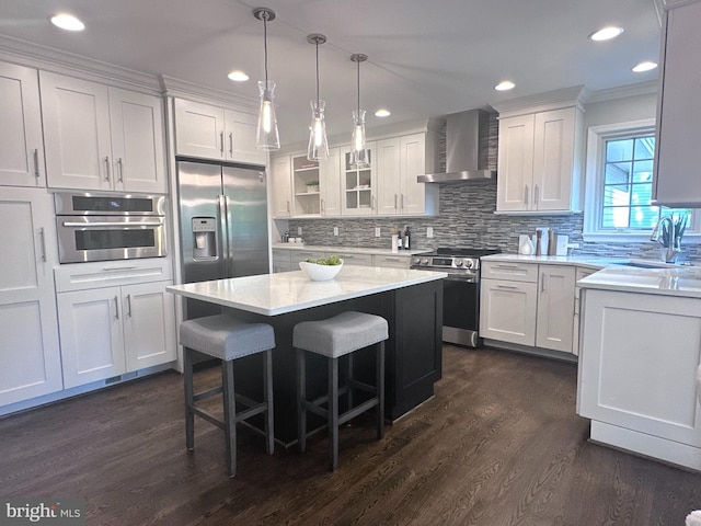 kitchen featuring dark wood-type flooring, wall chimney exhaust hood, white cabinetry, a sink, and appliances with stainless steel finishes
