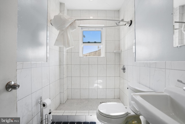 bathroom featuring a sink, tile walls, toilet, and tiled shower