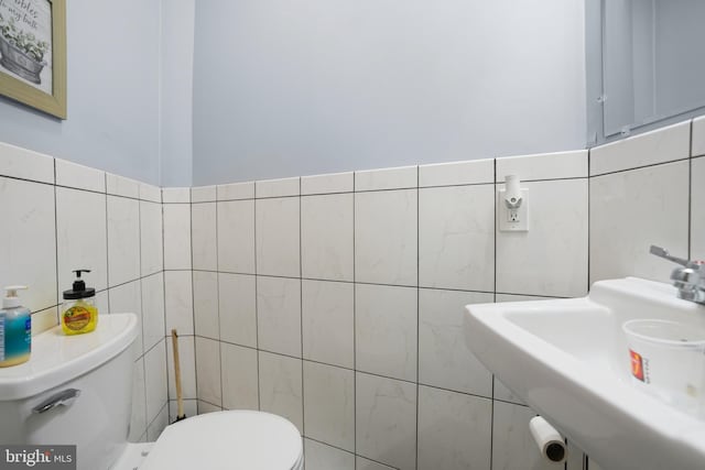 bathroom featuring a sink, tile walls, and toilet