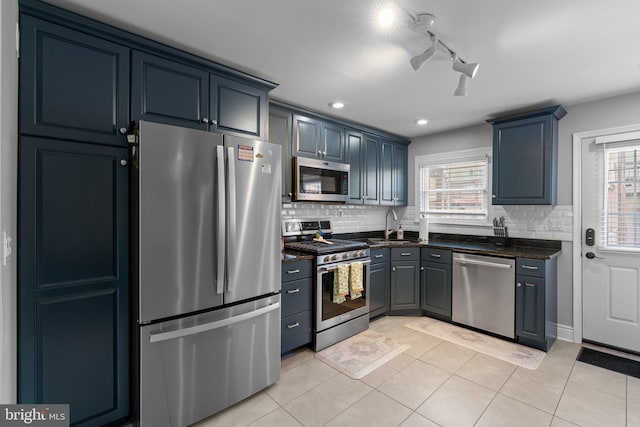 kitchen with decorative backsplash, a sink, dark stone countertops, light tile patterned floors, and stainless steel appliances