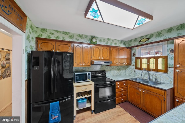 kitchen featuring under cabinet range hood, wallpapered walls, a sink, black appliances, and brown cabinetry