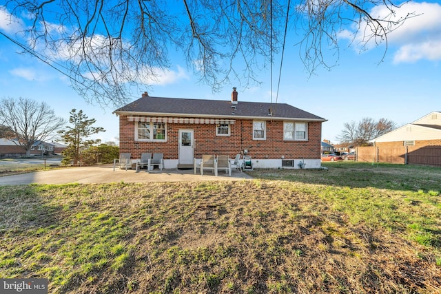back of house featuring a chimney, fence, brick siding, a patio, and a yard