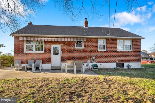 back of house with a chimney, brick siding, a shingled roof, a patio, and a lawn