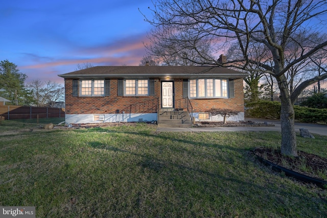 view of front of home featuring a chimney, brick siding, fence, and a lawn