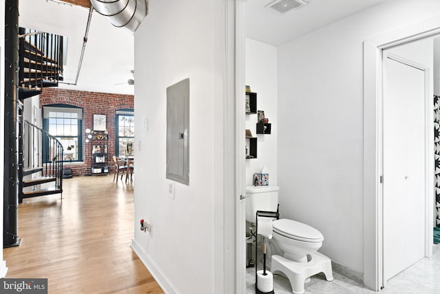 bathroom with electric panel, toilet, a ceiling fan, brick wall, and visible vents
