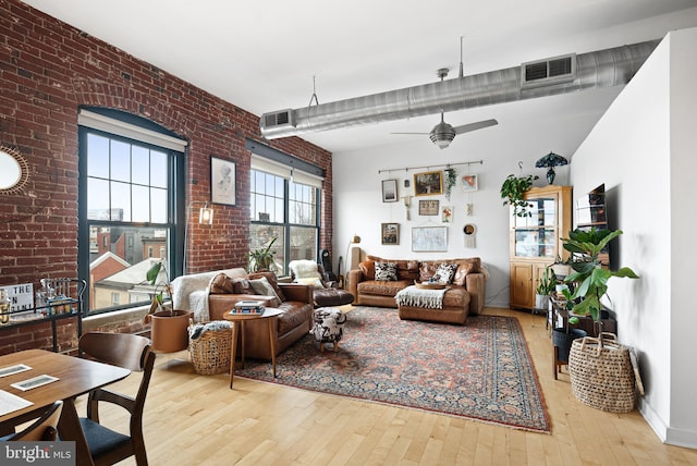 living area with visible vents, a ceiling fan, brick wall, and wood-type flooring