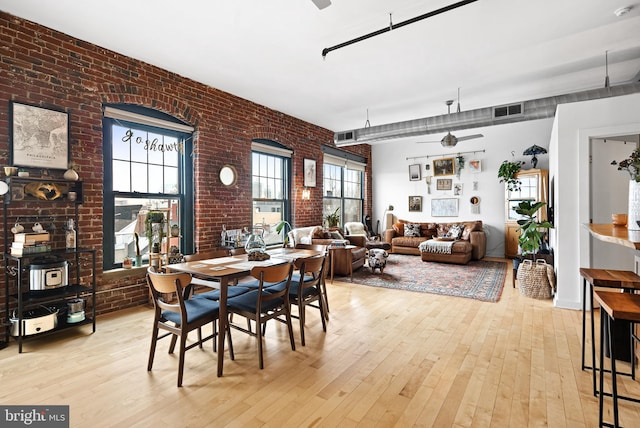 dining space featuring plenty of natural light, visible vents, brick wall, and wood-type flooring