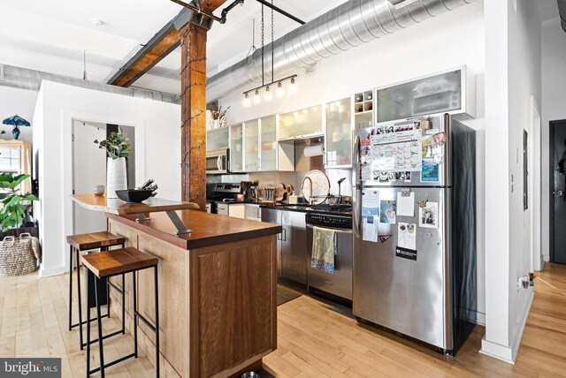 kitchen with a breakfast bar, a sink, light wood finished floors, appliances with stainless steel finishes, and glass insert cabinets