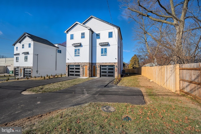 view of front of house with an attached garage, fence, driveway, and stone siding