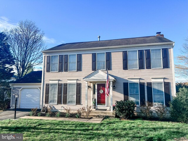 colonial house with a chimney, an attached garage, aphalt driveway, and a front lawn