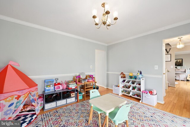 recreation room featuring ornamental molding, baseboards, a notable chandelier, and wood finished floors