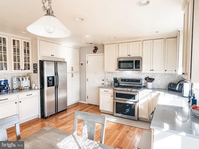 kitchen with light wood-style flooring, tasteful backsplash, glass insert cabinets, light stone counters, and appliances with stainless steel finishes