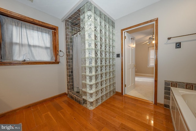 bathroom featuring a tile shower, baseboards, a bath, and wood finished floors