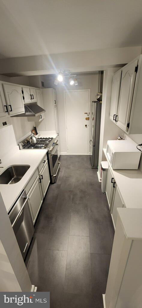 kitchen featuring white cabinets, a sink, light countertops, under cabinet range hood, and appliances with stainless steel finishes