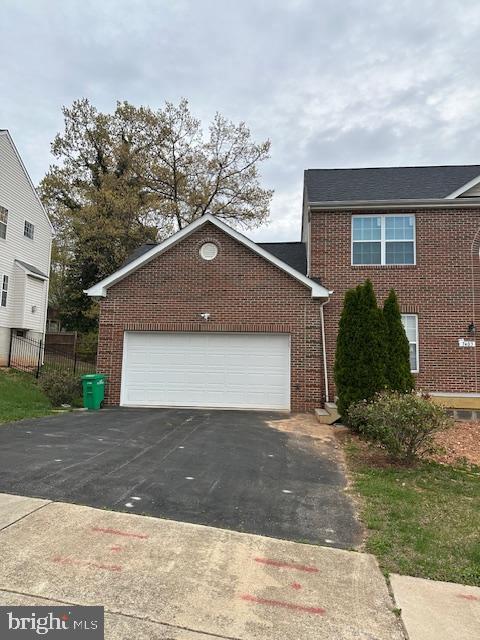 traditional home with aphalt driveway, a garage, fence, and brick siding