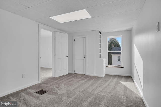 carpeted empty room featuring baseboards, visible vents, and a paneled ceiling