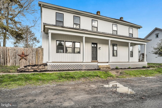 view of front of home featuring fence, a chimney, and covered porch