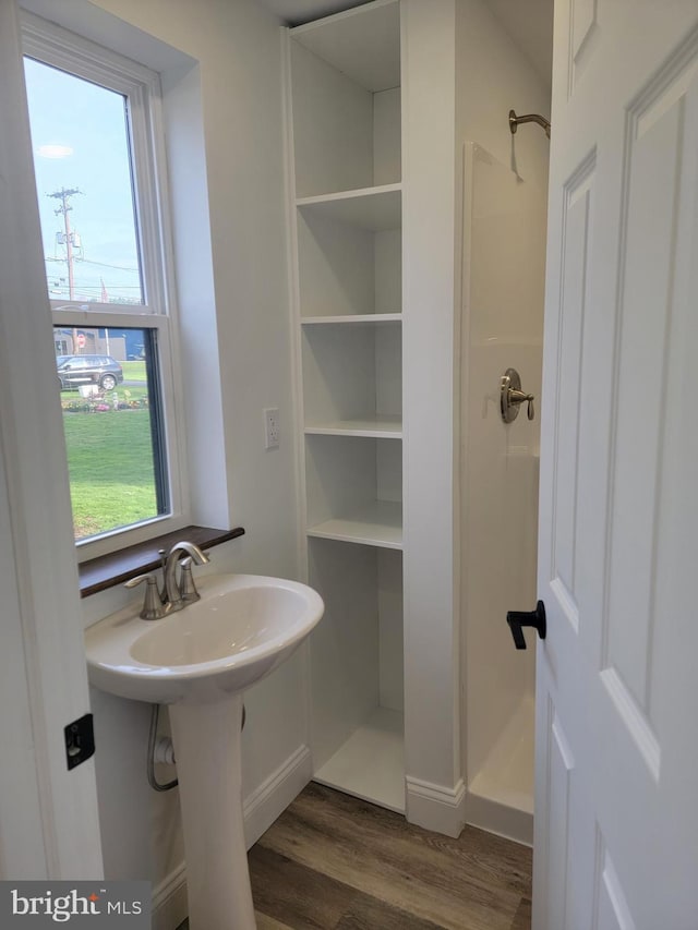 bathroom featuring a shower, wood finished floors, a sink, and baseboards