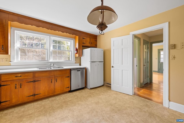 kitchen with light countertops, freestanding refrigerator, a sink, dishwasher, and brown cabinetry