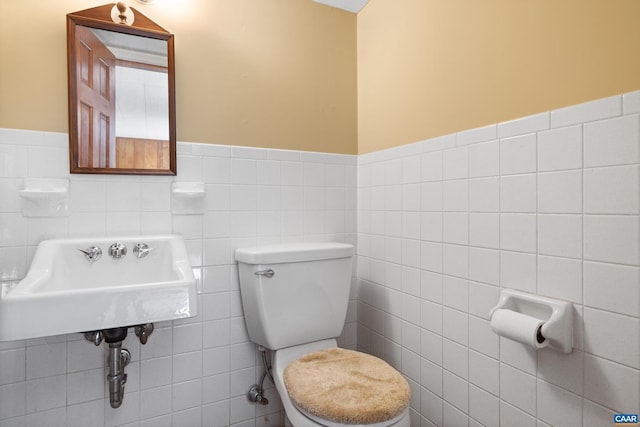 bathroom featuring a wainscoted wall, tile walls, toilet, and a sink