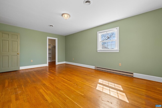 spare room featuring wood finished floors, baseboards, a baseboard heating unit, and visible vents
