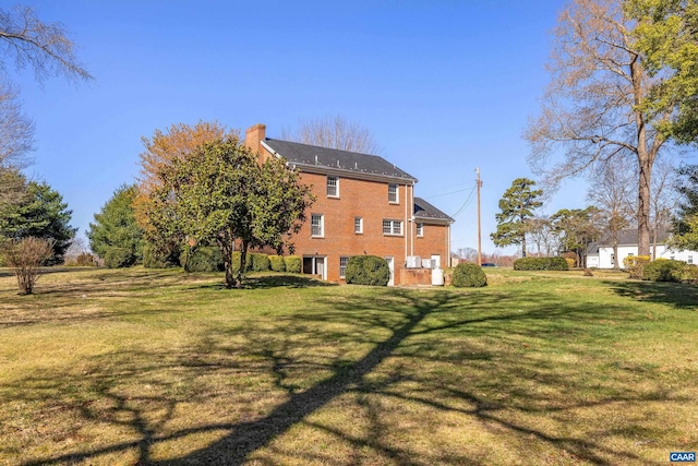 exterior space featuring brick siding, a yard, and a chimney