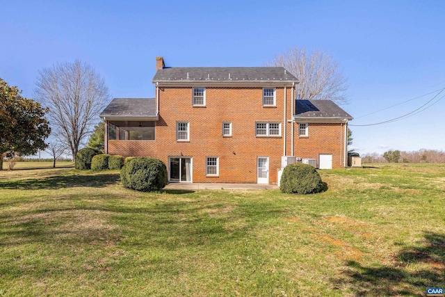back of house with a lawn, a sunroom, a chimney, and brick siding