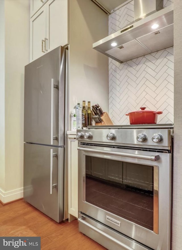 kitchen featuring tasteful backsplash, light wood-style floors, wall chimney range hood, and stainless steel appliances