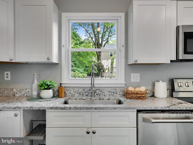 kitchen with appliances with stainless steel finishes, a sink, white cabinets, and light stone countertops