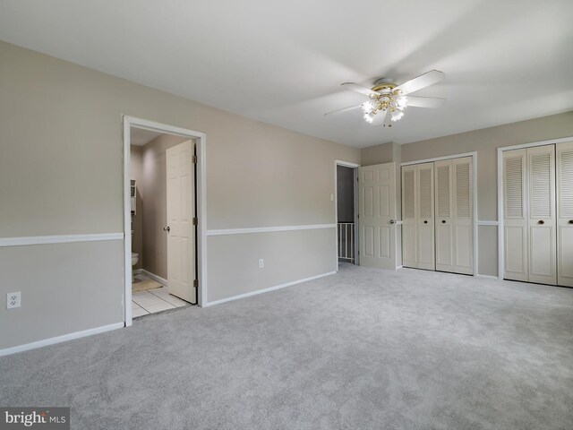 unfurnished bedroom featuring carpet flooring, two closets, baseboards, ensuite bathroom, and ceiling fan