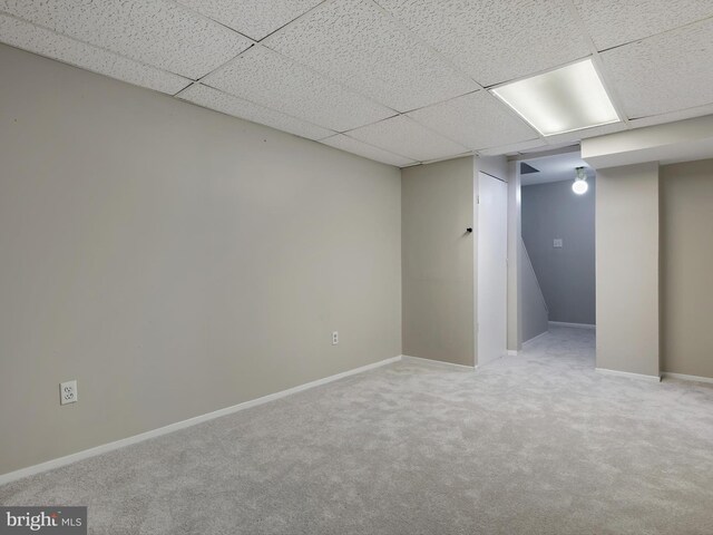 finished below grade area featuring carpet flooring, a paneled ceiling, and baseboards