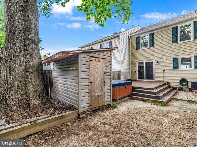 rear view of house featuring a hot tub, a shed, an outdoor structure, a wooden deck, and central AC