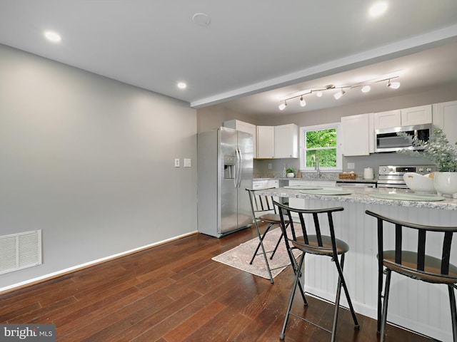 kitchen featuring stainless steel appliances, a kitchen breakfast bar, white cabinets, dark wood-style floors, and a peninsula
