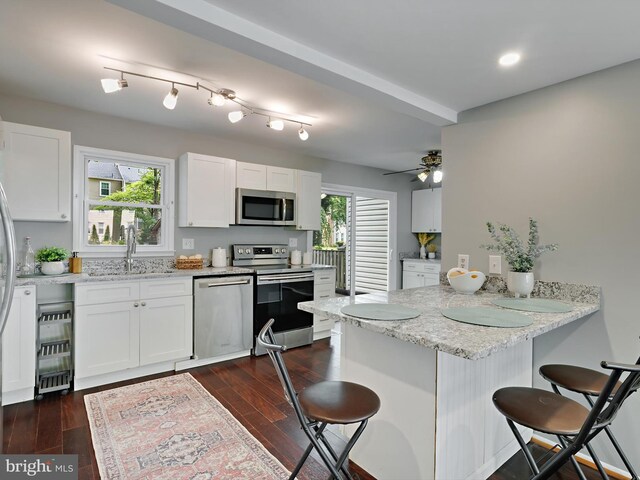 kitchen featuring appliances with stainless steel finishes, a peninsula, a kitchen breakfast bar, a sink, and white cabinetry
