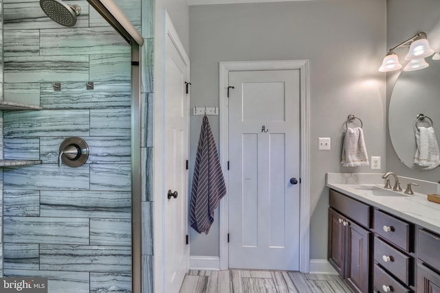 bathroom with baseboards, vanity, and a tile shower