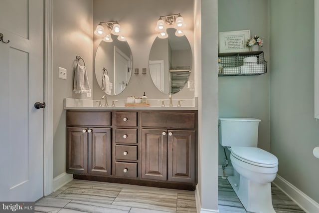 full bath with toilet, a sink, double vanity, and baseboards