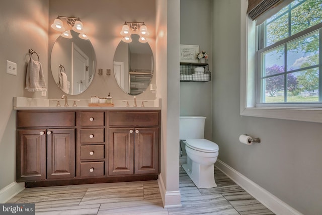 bathroom featuring baseboards, a sink, double vanity, and toilet