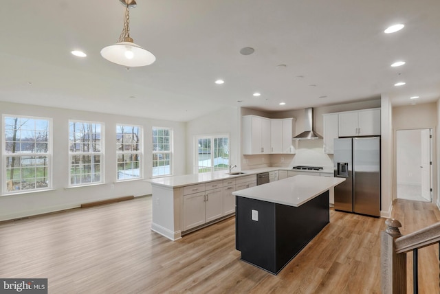 kitchen with light countertops, a center island, a sink, appliances with stainless steel finishes, and wall chimney exhaust hood