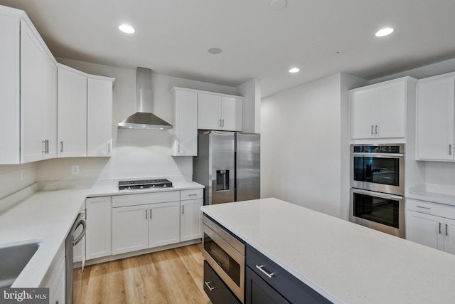 kitchen with wall chimney range hood, white cabinets, light countertops, and appliances with stainless steel finishes