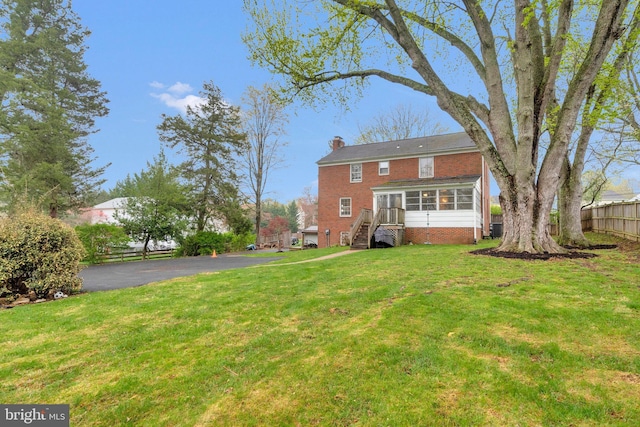 back of house featuring a sunroom, a yard, fence, brick siding, and a chimney