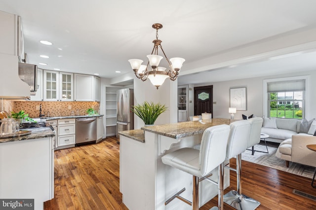 kitchen with glass insert cabinets, an inviting chandelier, visible vents, a kitchen breakfast bar, and appliances with stainless steel finishes