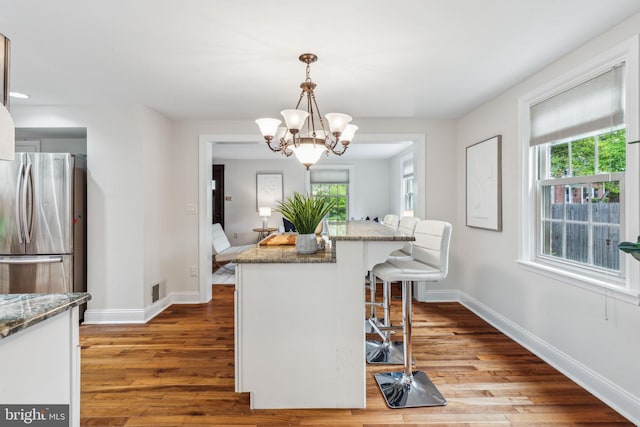 kitchen with freestanding refrigerator, wood finished floors, a kitchen breakfast bar, and a notable chandelier