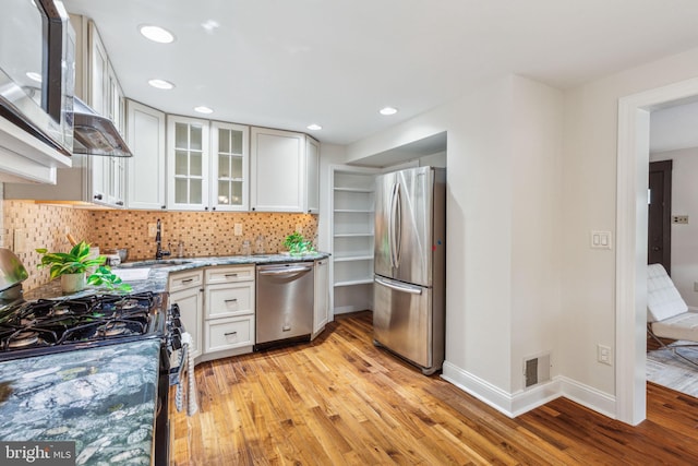 kitchen featuring a sink, light wood-style floors, baseboards, appliances with stainless steel finishes, and decorative backsplash